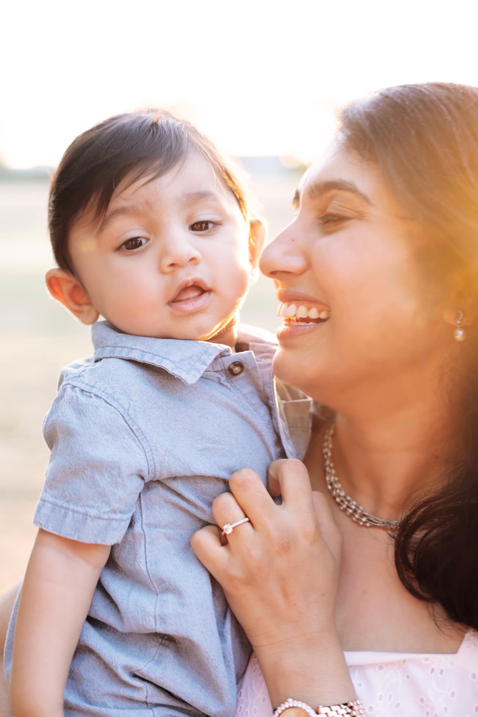 A mother laughs closely with her toddler son, golden hour light behind them.