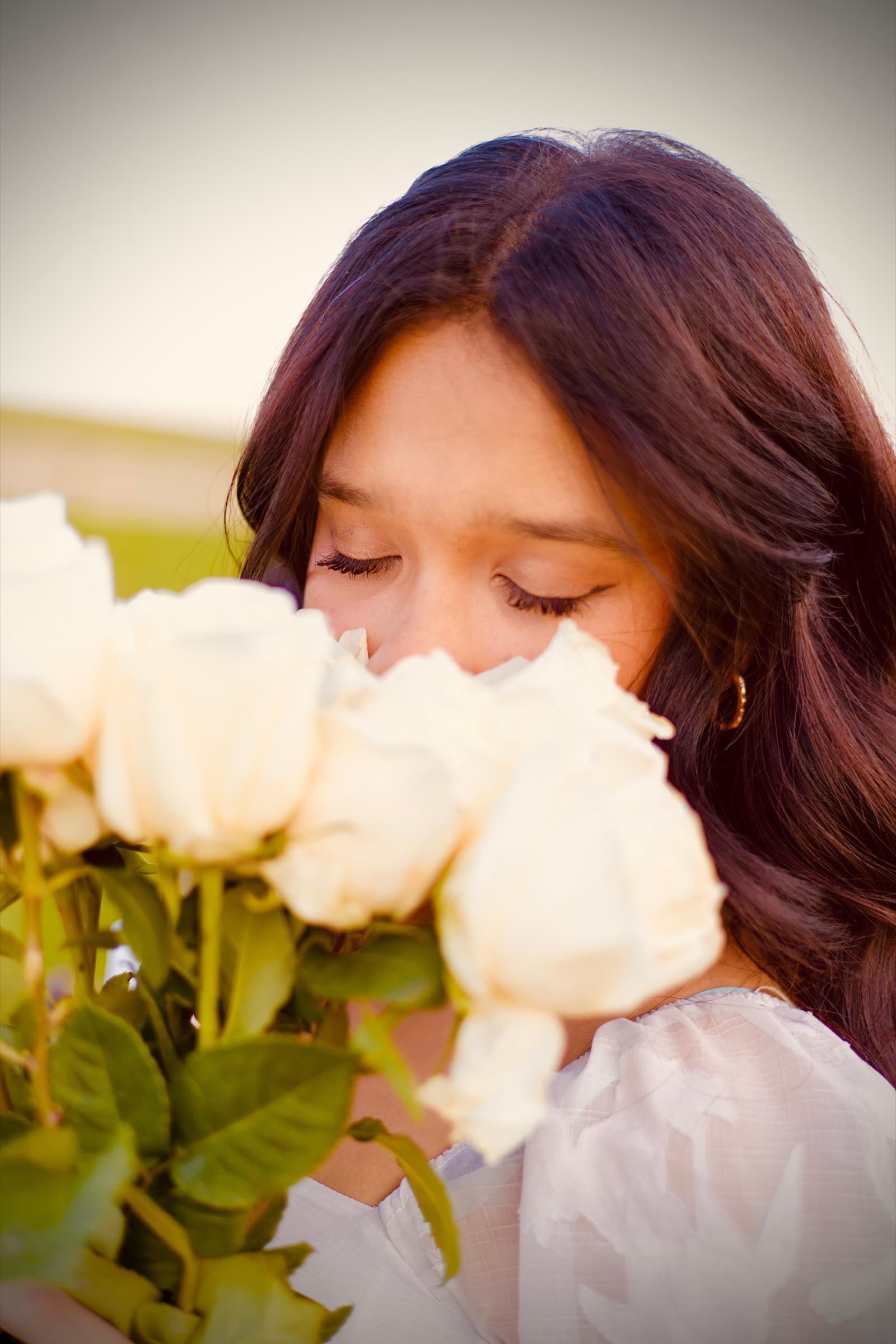 Close-up of a young woman smelling a bouquet of white roses, warm golden-hour light in her hair.